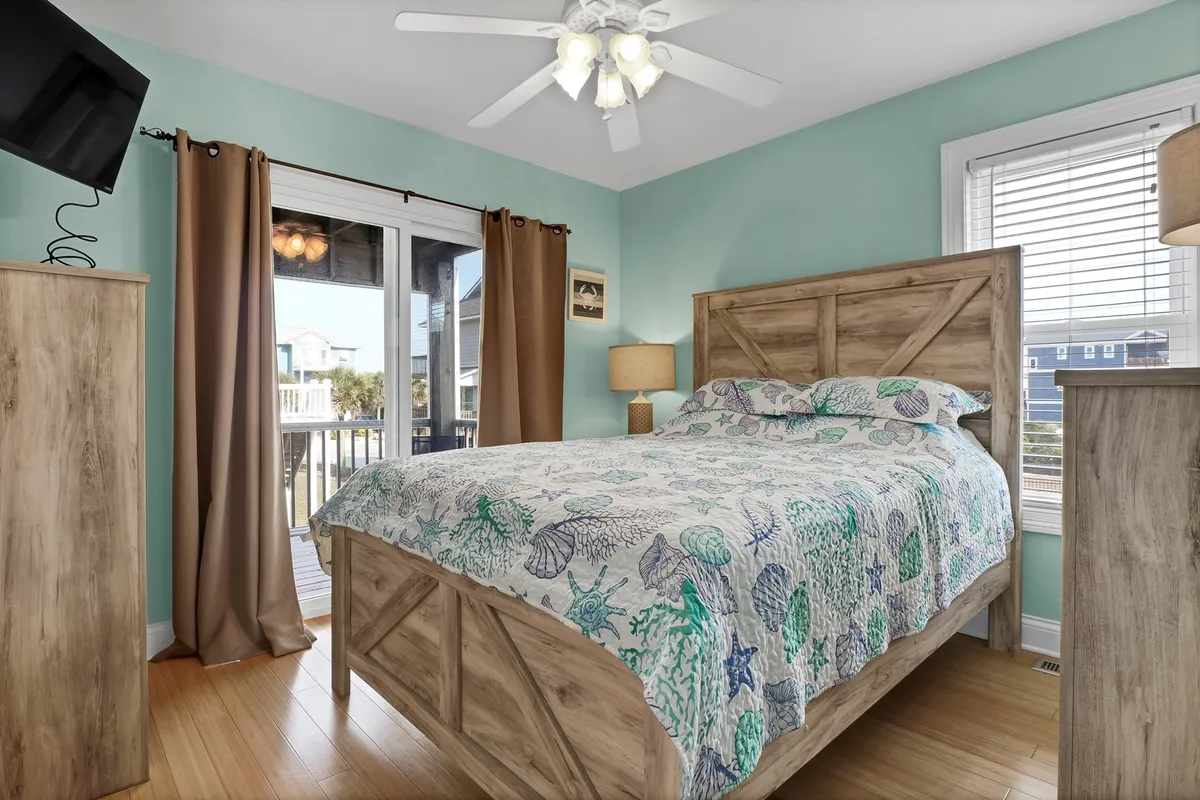 A cozy bedroom featuring a bed with vibrant, colorful bedding, ample wooden furnishings, and a large window allowing sunshine to fill the space. The decor is cheerful yet calming, ideal for a restful atmosphere.
