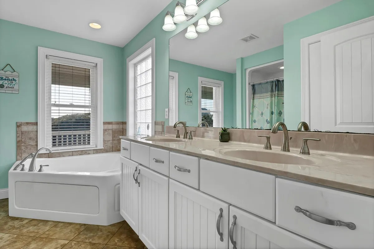 An inviting, spa-like bathroom with double vanity sinks, a pristine bathtub, and expansive windows that flood the space with natural light. The design is modern and relaxing, offering a luxurious spot to unwind after beach adventures.