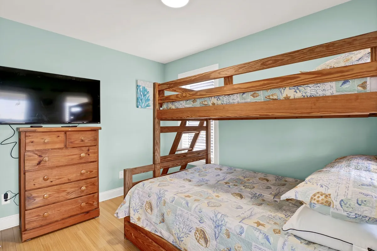 A playful and inviting bunk room with a Twin over Full bunk bed, a flat-screen TV, a wooden dresser, and bright, colorful bedding. The room feels fun and cozy, perfect for children or friends sharing the space.