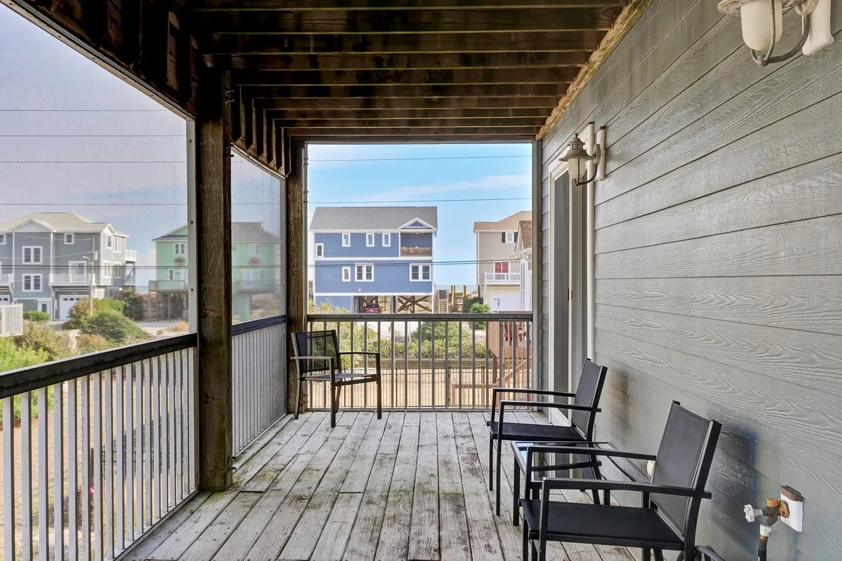 A wooden deck furnished with chairs, overlooking a scenic neighborhood of beach houses. The space is perfect for relaxing with a book, enjoying morning coffee, or hosting casual group get-togethers as the sun sets.
