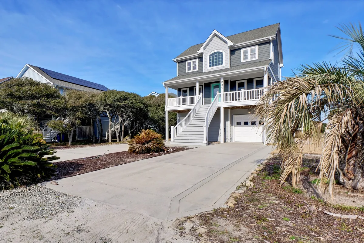 The inviting exterior of a private home with stairs leading to the entrance, palm tree landscaping, and a spacious driveway. The porch suggests spaces for family gatherings and outdoor relaxation, highlighting the welcoming, home-away-from-home vibe.