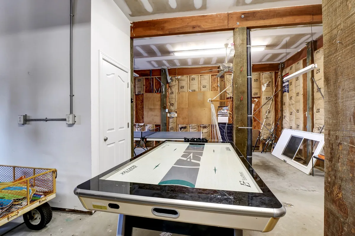 This image captures a casual and relaxed interior setting featuring an air hockey table, visible structural beams, and an open door hinting at an entryway. The room is set up for fun with ample space for friendly competitions, and the atmosphere invites both kids and adults to play.