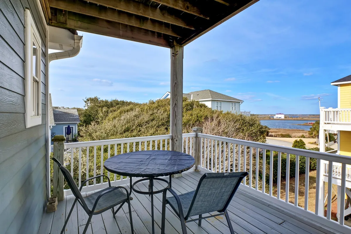 An exterior shot featuring a round table and outdoor chairs set against a serene water view. The scene evokes calm mornings, sunset watching, and social gatherings, providing a welcoming space for group interactions.