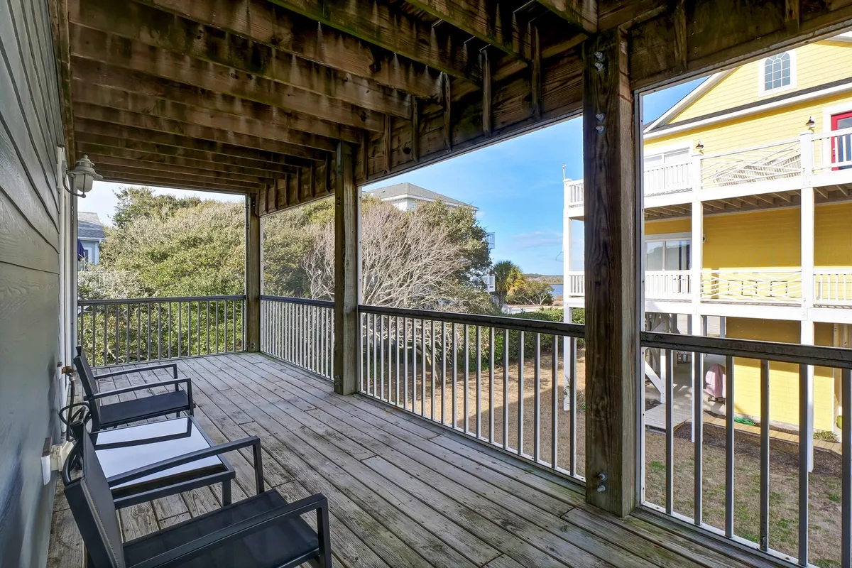 A peaceful exterior deck furnished with comfortable chairs and surrounded by trees, providing a secluded spot to relax, socialize, or enjoy morning coffee while taking in the natural surroundings. The yellow house in the background adds a touch of cheerful color to the scene.