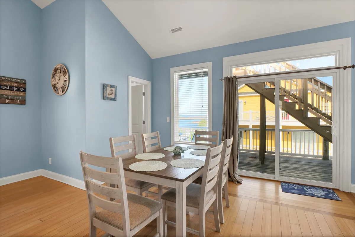 A dining table positioned by large windows allowing plenty of sunlight to stream in, with views to the outdoors. The room exudes comfort and is set up for family meals, casual gatherings, or enjoying morning coffee with a view.