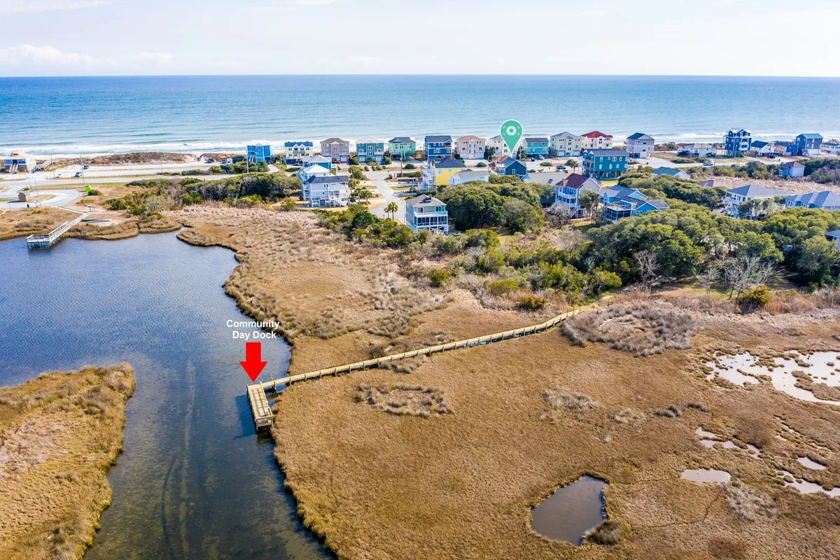 A wide view of the community day dock surrounded by coastal homes, with an expansive view of the ocean and marshland. The scene captures the peaceful ambiance of sunset gatherings and nature exploration, highlighting the area's waterfront amenities.