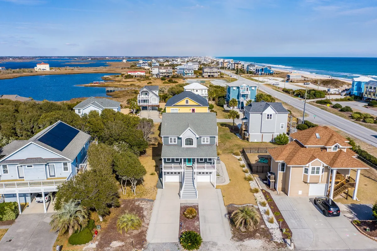 A classic beachfront property set amid other nearby houses, with the coastal landscape and the ocean just beyond. The image captures the relaxed mood of seaside living and the social possibilities of the surroundings.